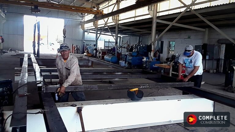 Workers assembling a large steel frame in a fabrication shop, with Complete Combustion logo in the bottom right.